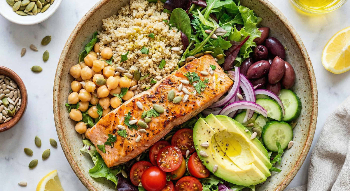 a bowl on a table with chickpeas, quinoa, salmon, tomatoes, avocado and cucumbers in it
